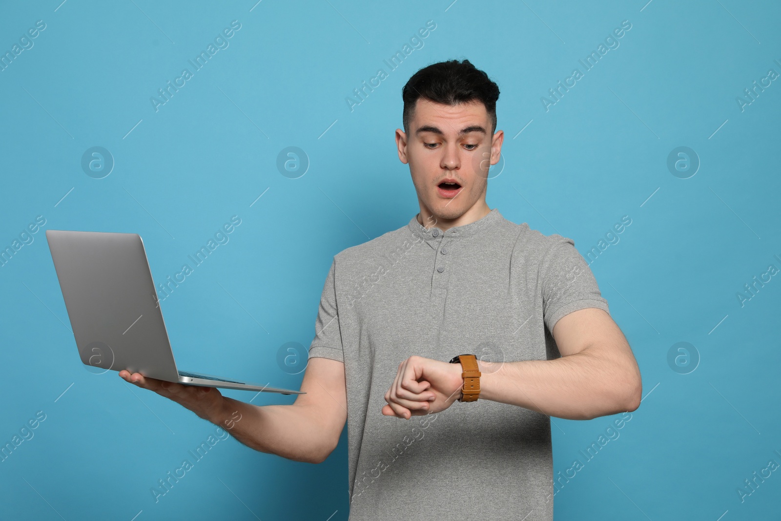 Photo of Emotional young man with laptop checking time on light blue background. Being late concept