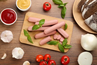 Fresh raw vegetarian sausages with basil and vegetables on wooden table, flat lay