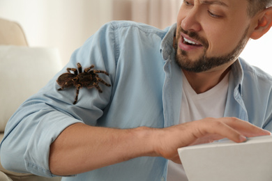 Photo of Scared man with tarantula at home, closeup. Arachnophobia (fear of spiders)