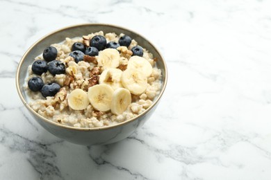 Photo of Tasty oatmeal with banana, blueberries, walnuts and milk served in bowl on white marble table, space for text