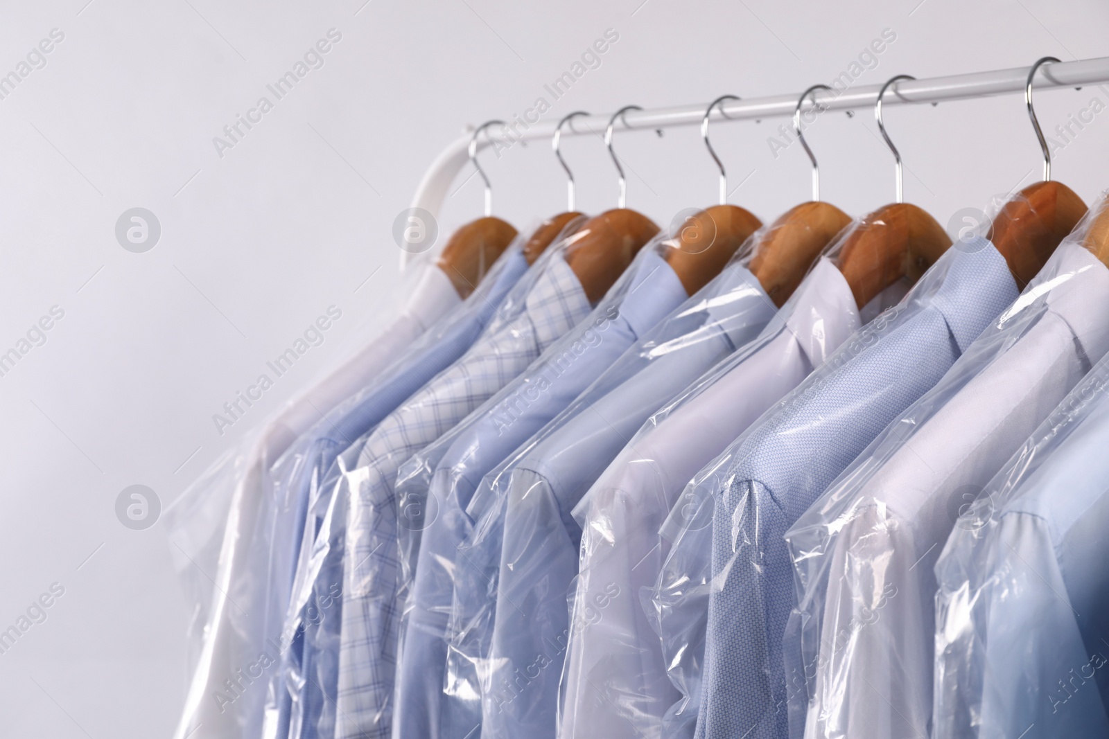 Photo of Hangers with shirts in dry cleaning plastic bags on rack against light background