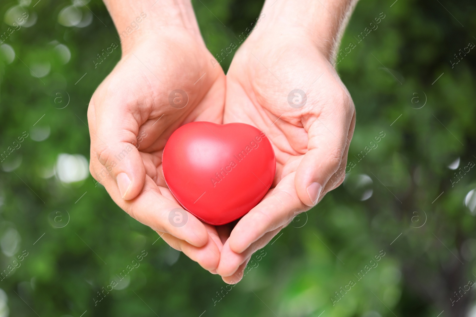 Photo of Young man holding red heart on blurred green background, closeup. Donation concept