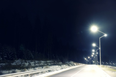 Night landscape with illuminated road and forest in winter