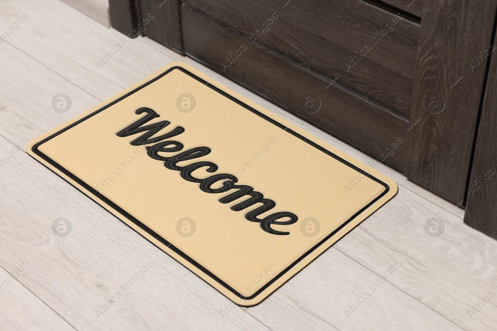 Photo of Beige doormat with word Welcome on white floor near entrance