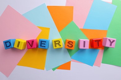 Photo of Word Diversity made of cubes with letters and colorful paper sheets on white background, flat lay