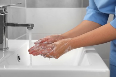 Photo of Doctor washing hands with water from tap in bathroom, closeup