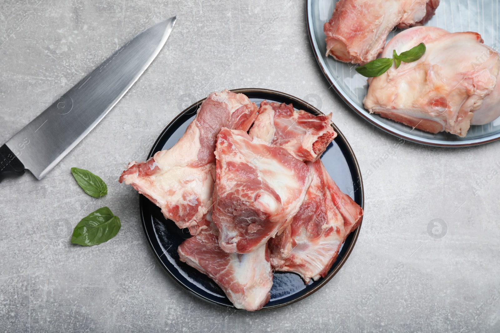 Photo of Plates with raw chopped meaty bones, basil and knife on grey table, top view