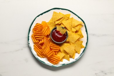 Photo of Plate with tasty ketchup, ridged and tortilla chips on marble table, top view