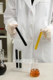 Laboratory worker holding test tubes with different types of crude oil at light marble table, closeup