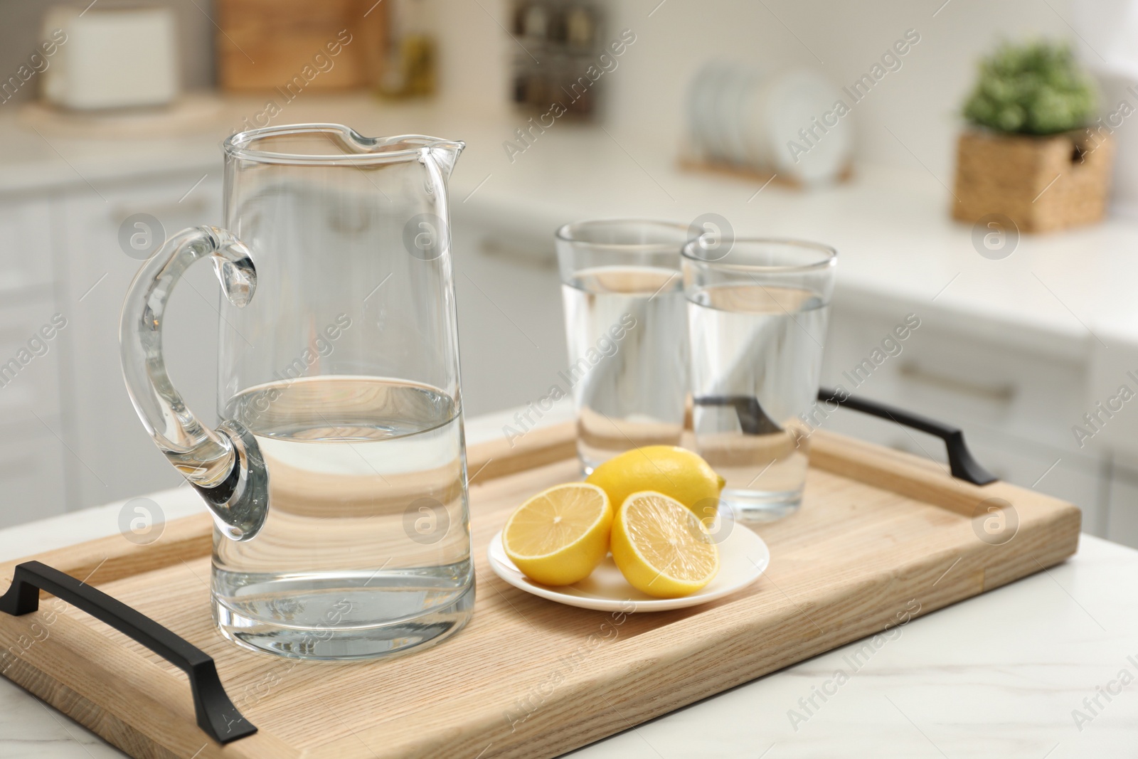 Photo of Jug, glasses with clear water and lemons on white table in kitchen