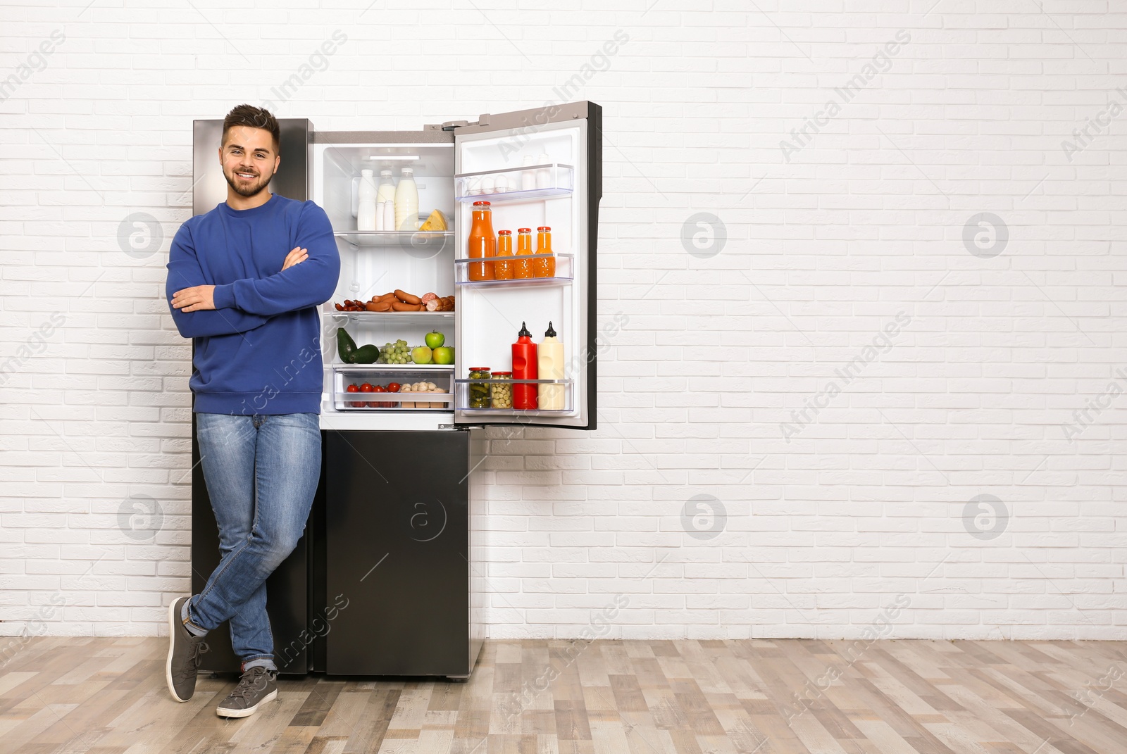 Photo of Happy young man near open refrigerator indoors, space for text