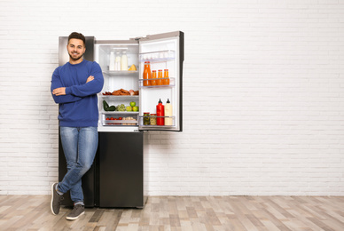 Happy young man near open refrigerator indoors, space for text