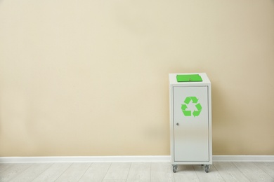 Trash bin with recycling symbol near color wall indoors. Space for text