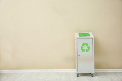 Photo of Trash bin with recycling symbol near color wall indoors. Space for text