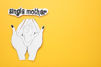 Being single mother concept. Woman holding her baby's feet made of paper on orange background, flat lay and space for text