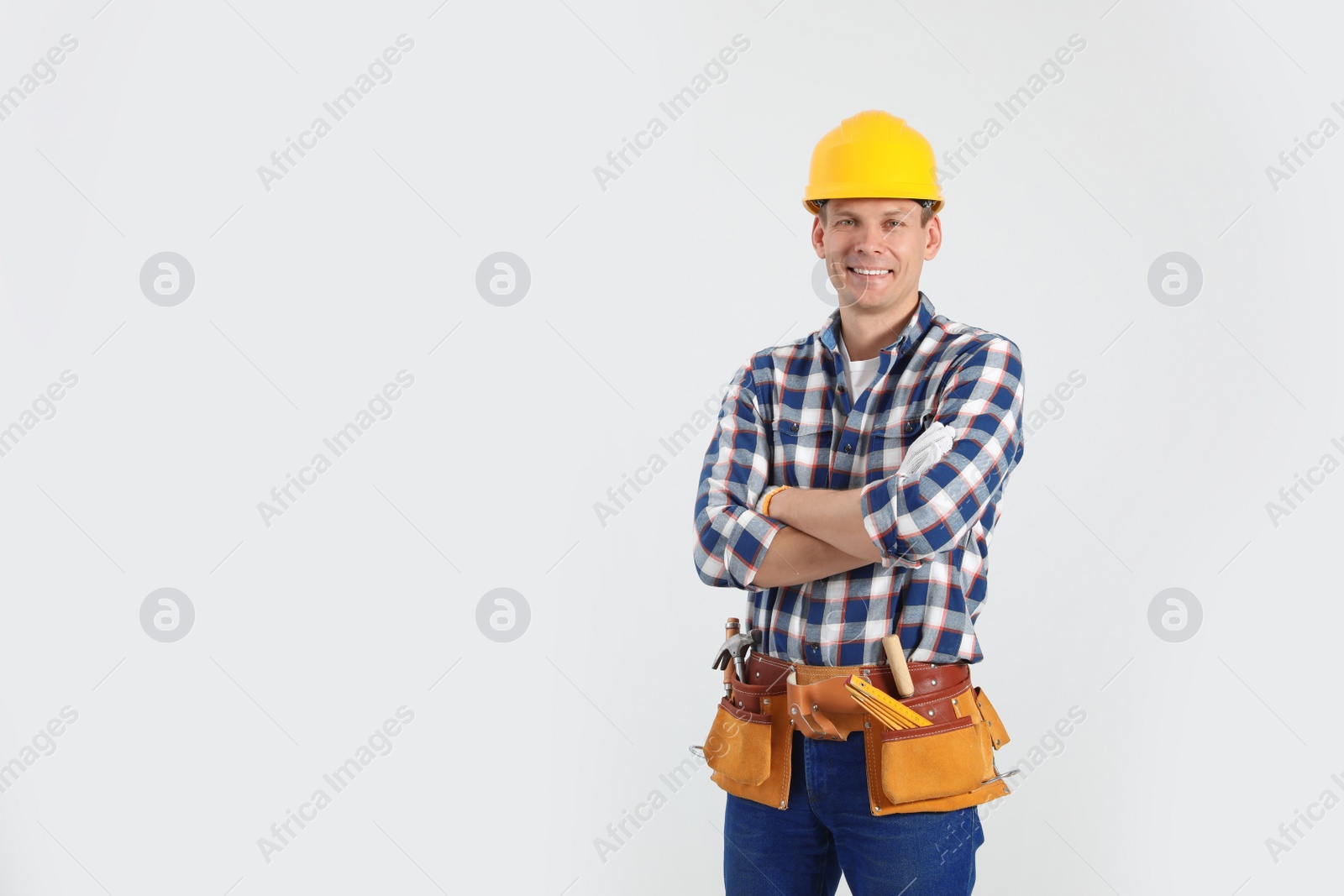 Photo of Handsome carpenter with tool belt on light background. Space for text
