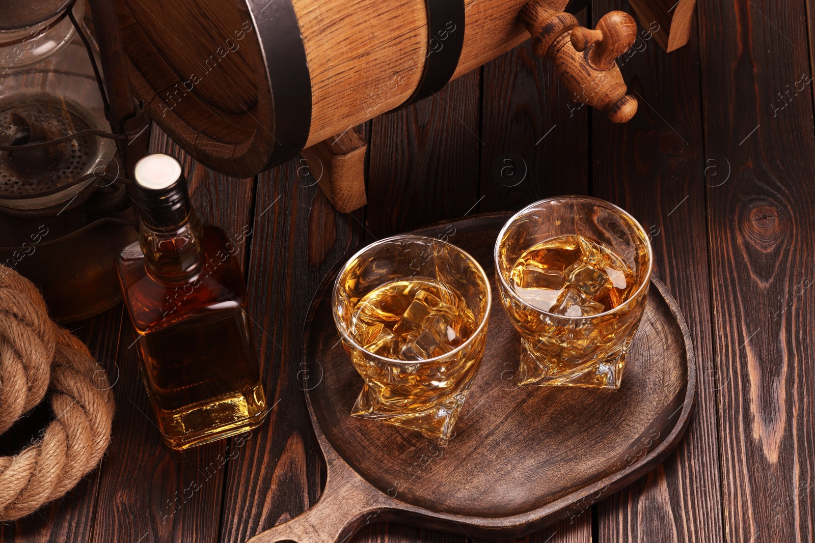 Photo of Whiskey with ice cubes in glasses, bottle and barrel on wooden table