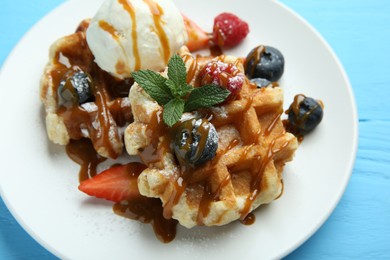 Photo of Delicious Belgian waffles with ice cream, berries and caramel sauce on light blue wooden table, closeup