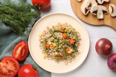 Photo of Delicious pearl barley with vegetables served on white tiled table, flat lay