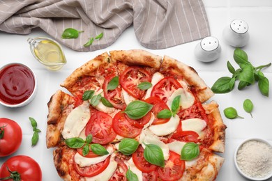 Photo of Delicious Caprese pizza and ingredients on white tiled table, flat lay