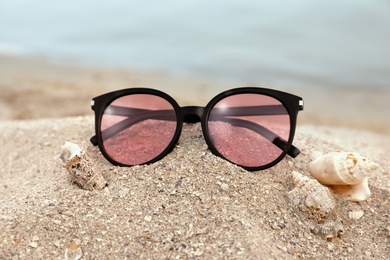 Stylish sunglasses and shells on sandy beach