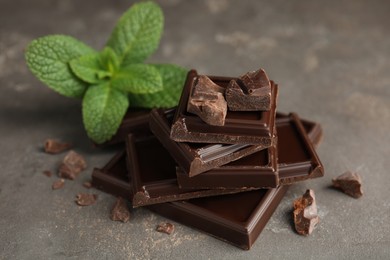Photo of Tasty dark chocolate pieces with mint on grey table