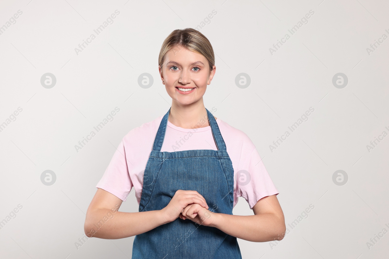 Photo of Beautiful young woman in denim apron on light grey background