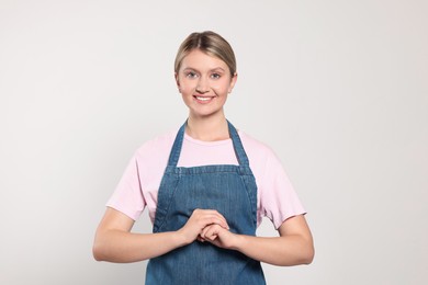 Beautiful young woman in denim apron on light grey background