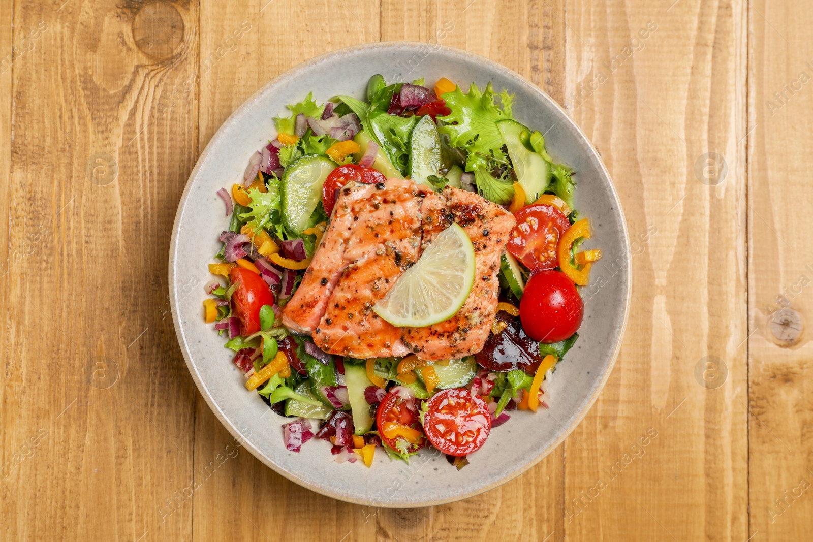 Photo of Bowl with tasty salmon , lemon and mixed vegetables on wooden table, top view