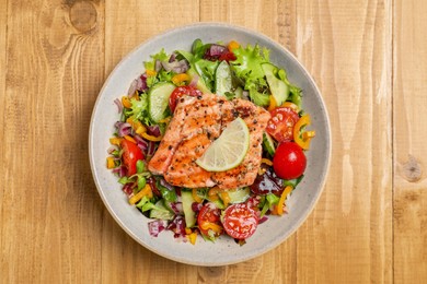 Photo of Bowl with tasty salmon , lemon and mixed vegetables on wooden table, top view