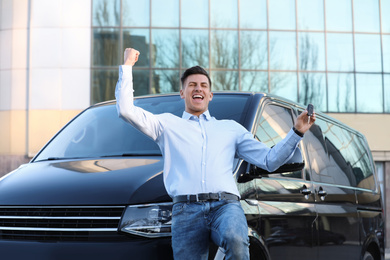 Excited man with key near car on city street. Buying new auto