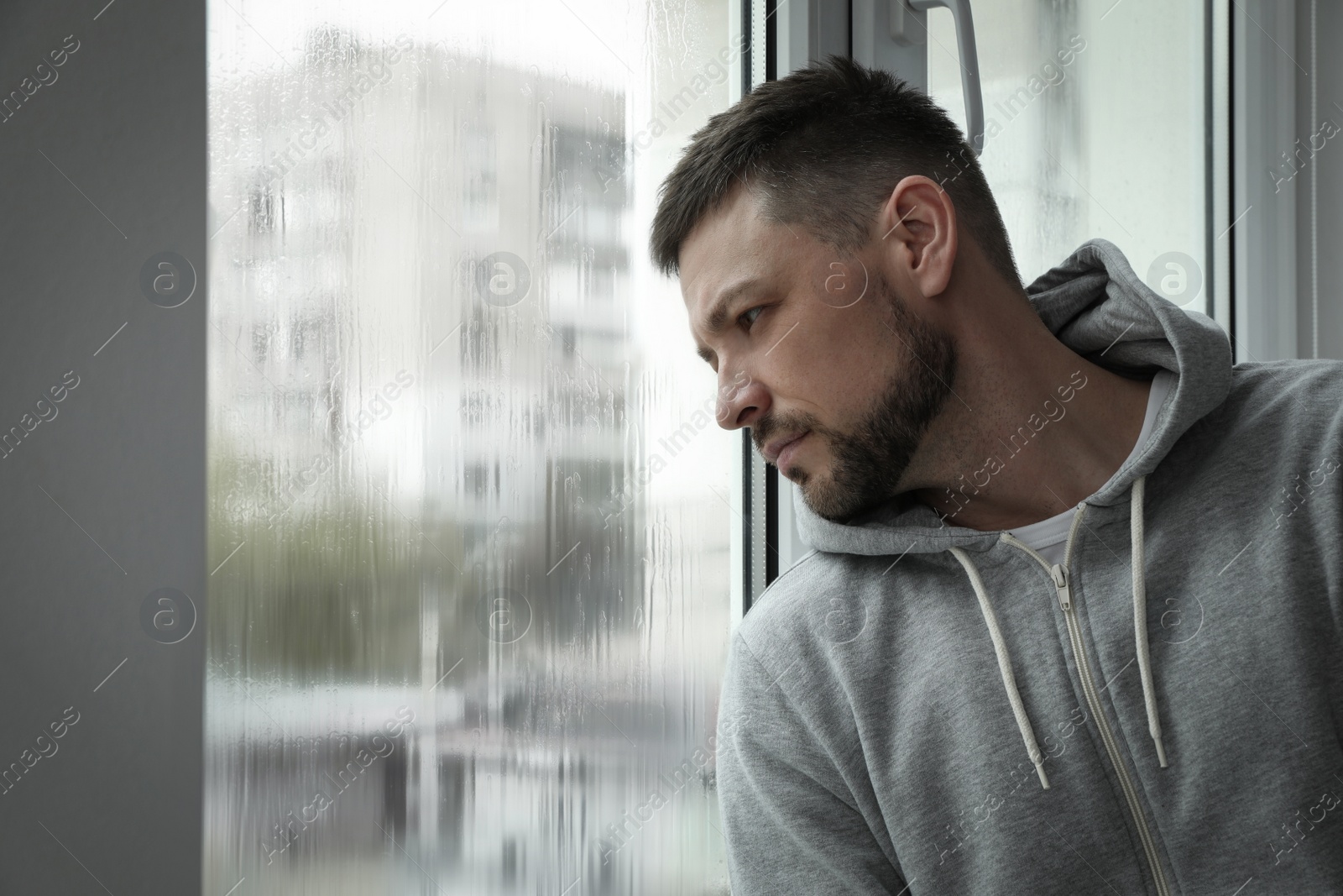 Photo of Depressed man near window at home. Space for text