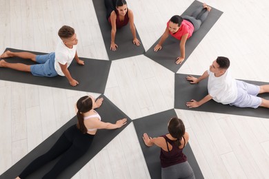 Group of people practicing yoga on mats indoors, above view
