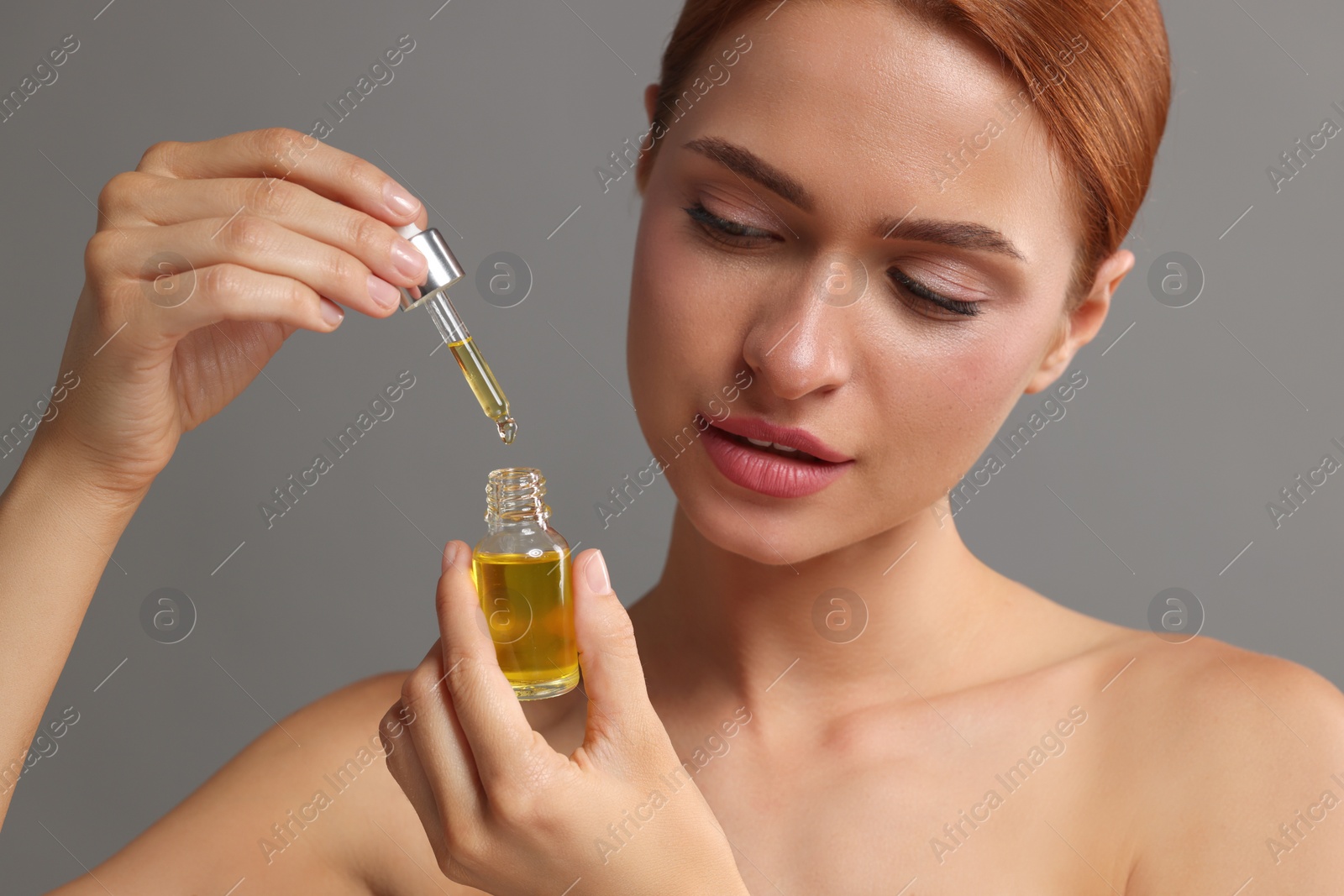 Photo of Beautiful young woman with bottle of cosmetic serum on grey background, closeup