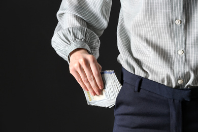 Woman putting bribe into pocket on black background, closeup