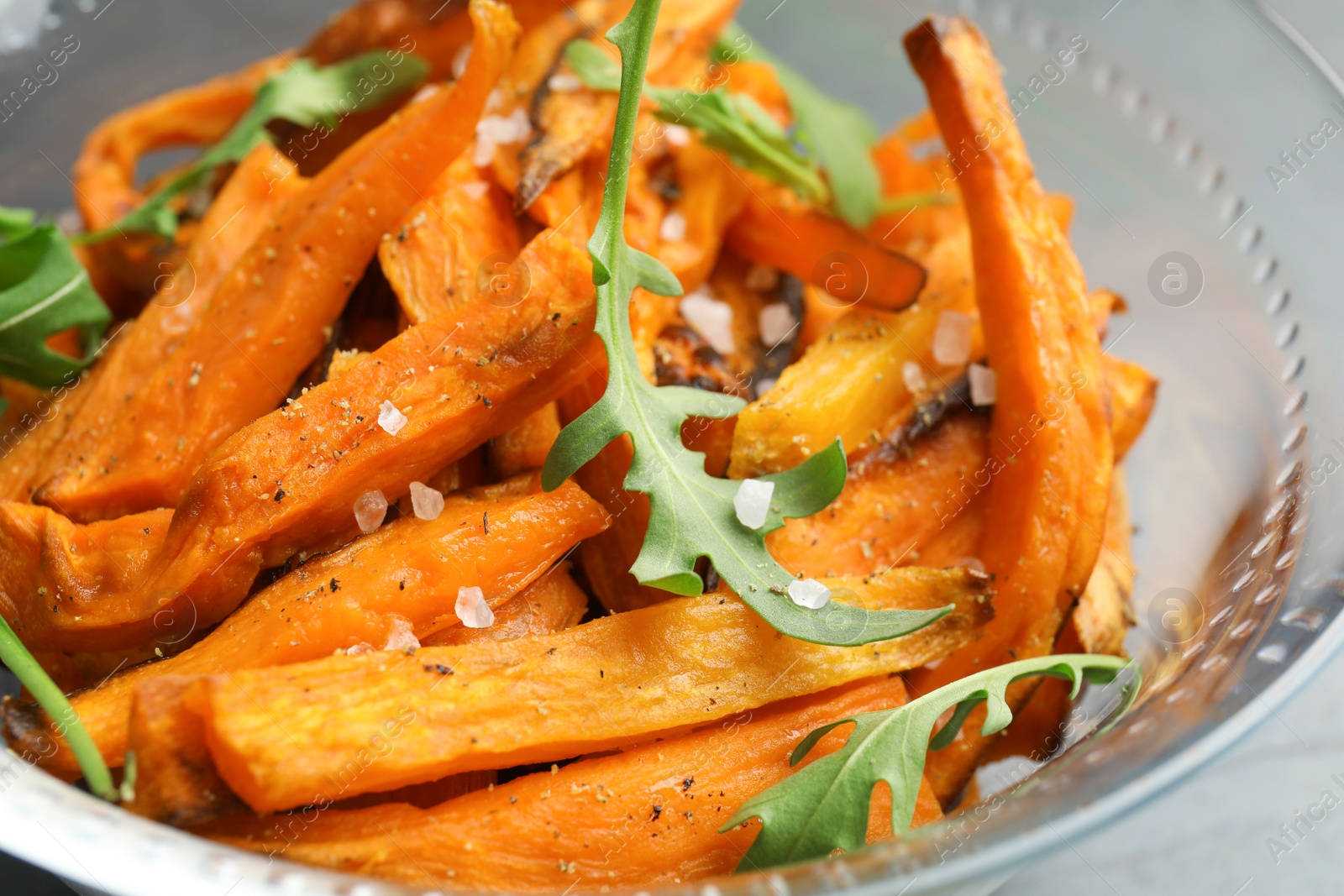 Photo of Glass bowl with baked sweet potato slices and arugula, closeup