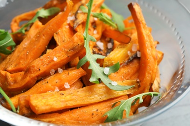 Photo of Glass bowl with baked sweet potato slices and arugula, closeup