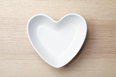 Heart shaped plate on wooden background, top view