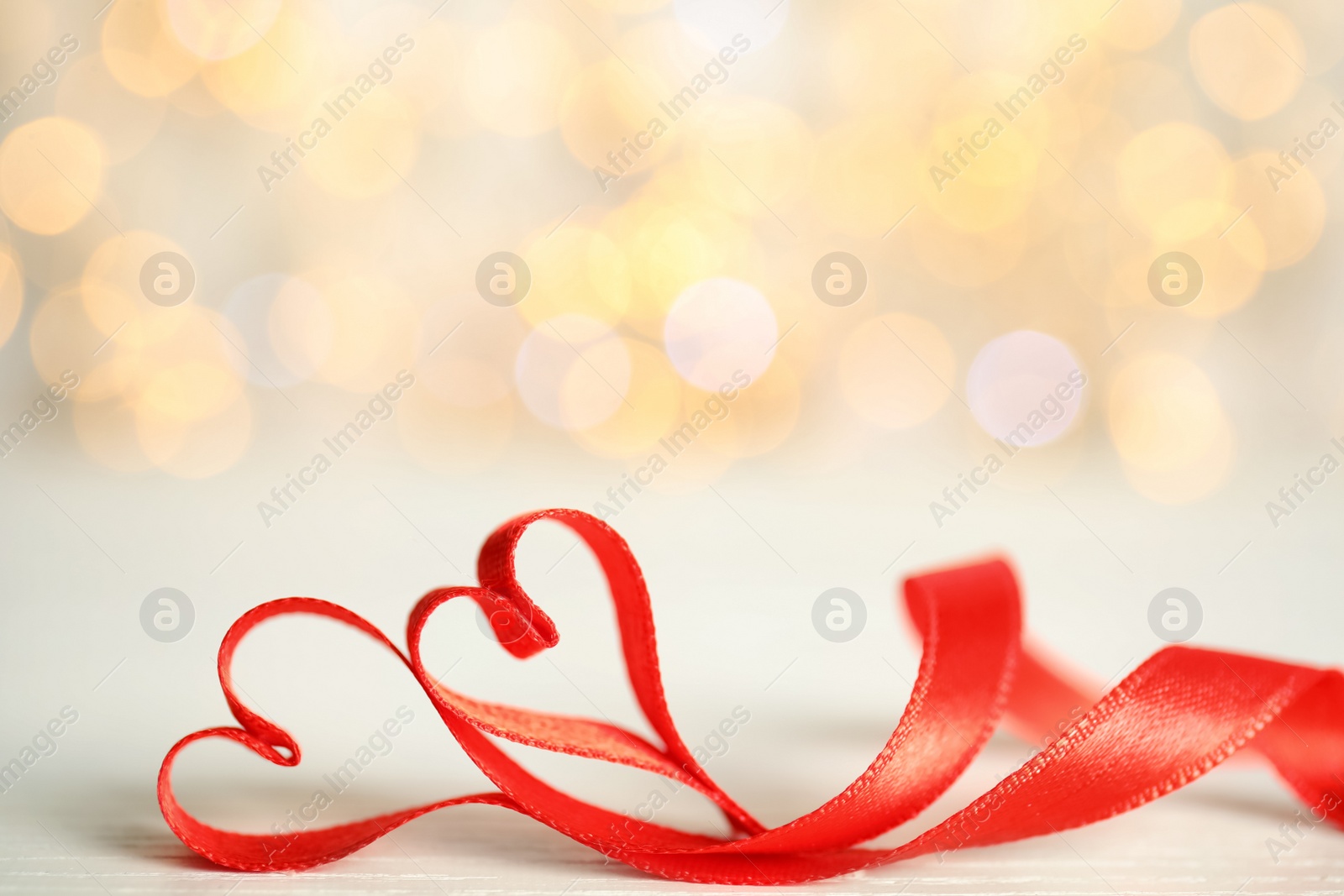 Photo of Two hearts made of red ribbon on table against blurred lights, space for text. St. Valentine's day card