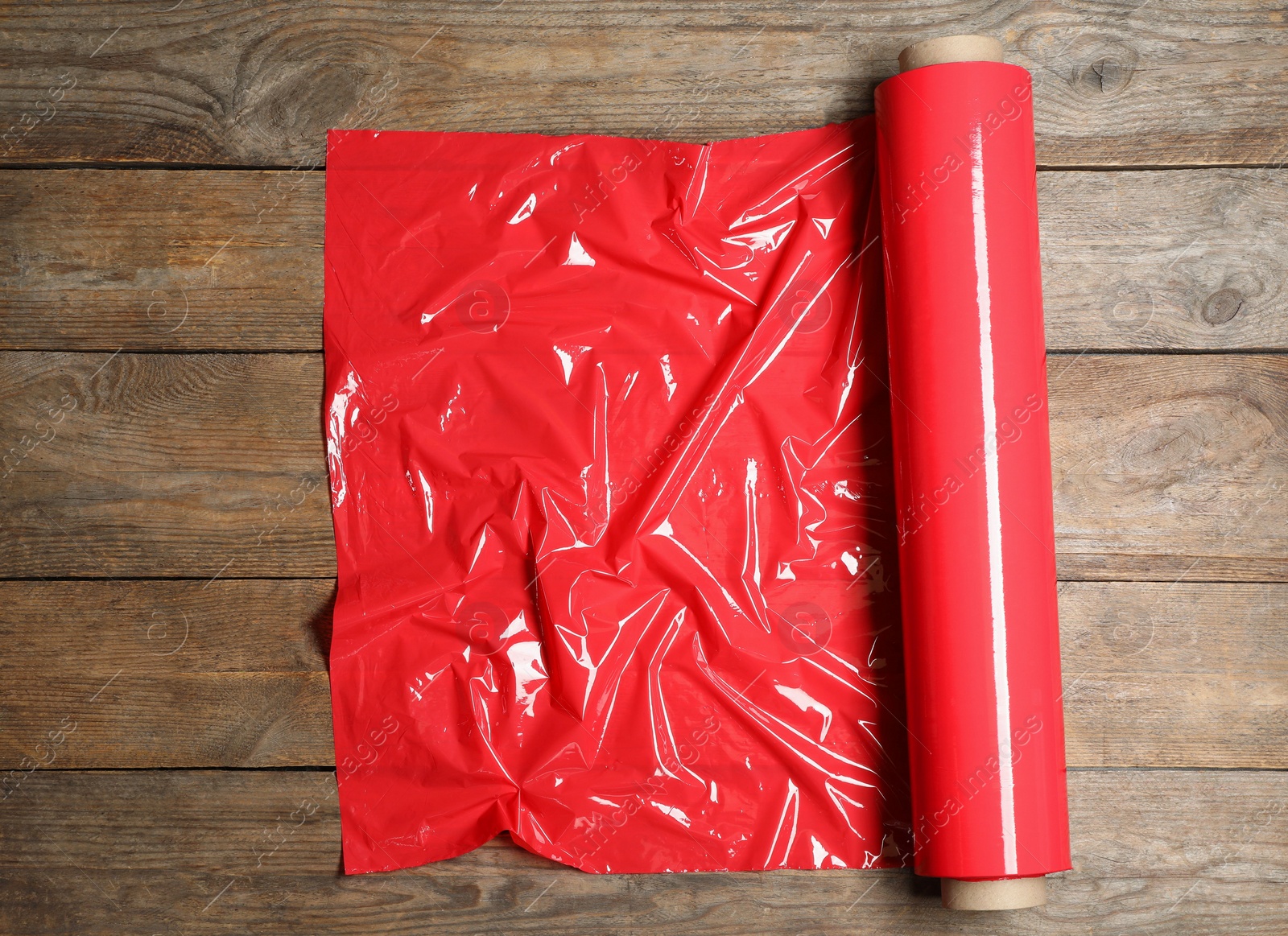 Photo of Roll of red plastic stretch wrap on wooden background, top view