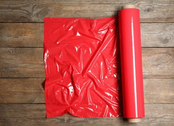 Photo of Roll of red plastic stretch wrap on wooden background, top view