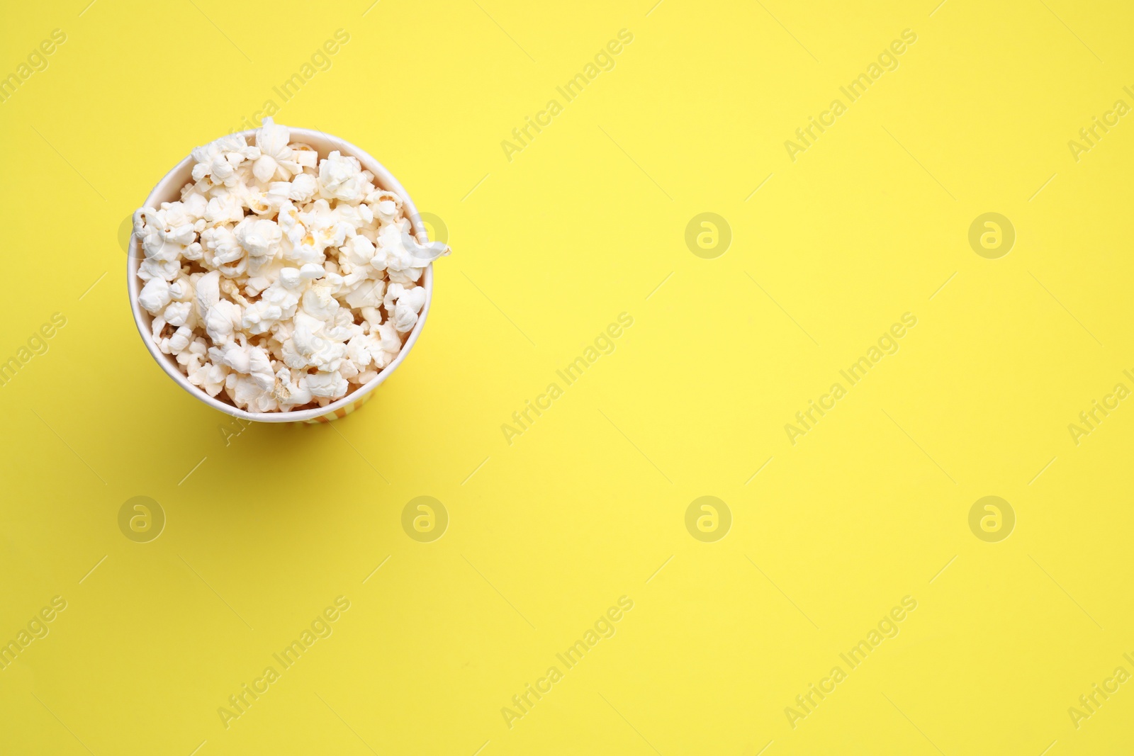 Photo of Paper cup with delicious popcorn on yellow background, top view. Space for text