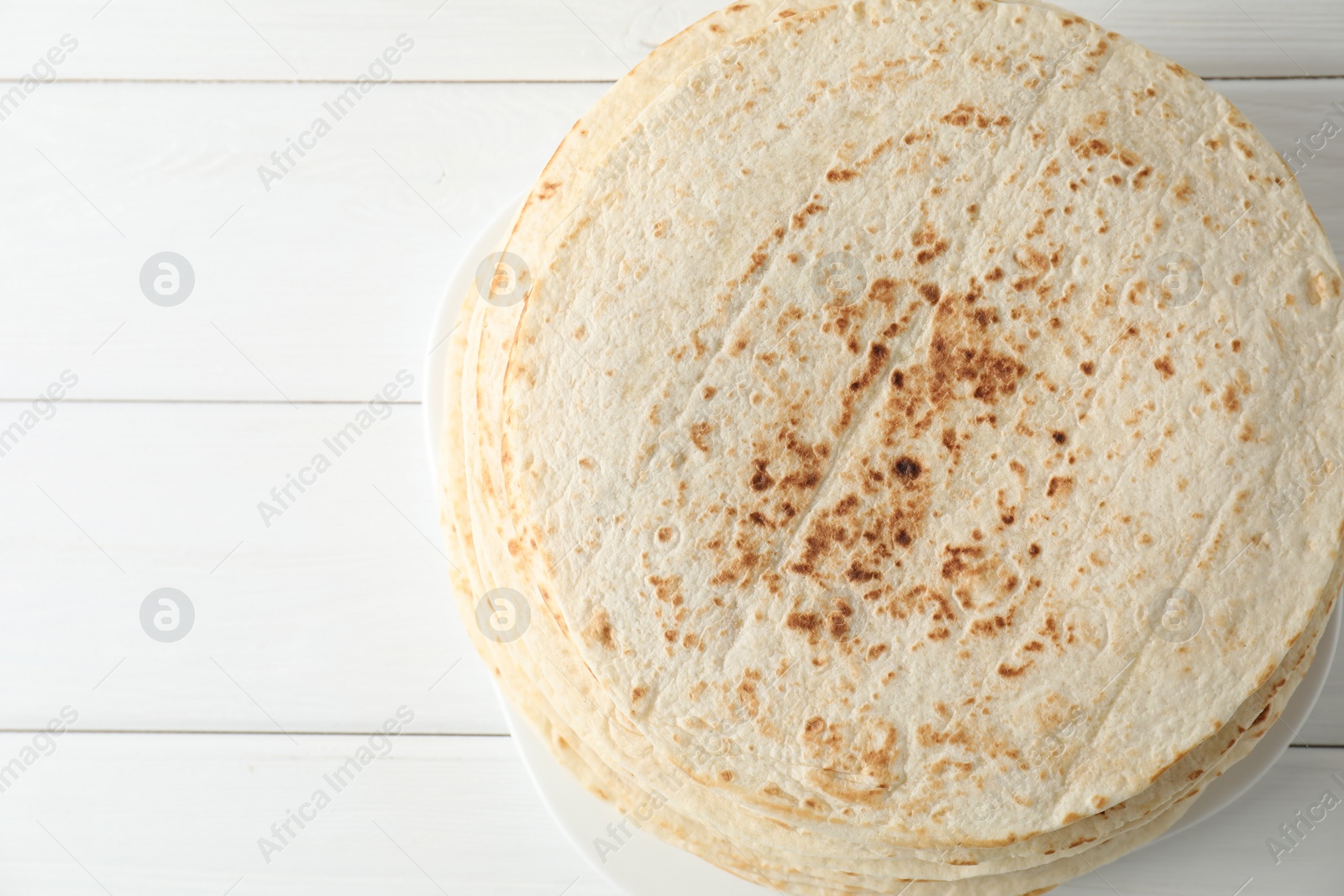 Photo of Stack of tasty homemade tortillas on white wooden table, top view. Space for text