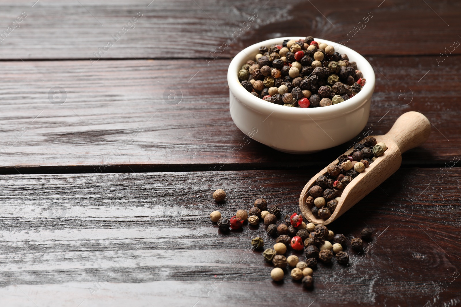 Photo of Aromatic spice. Different peppers in bowl and scoop on wooden table, space for text