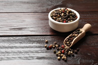 Aromatic spice. Different peppers in bowl and scoop on wooden table, space for text