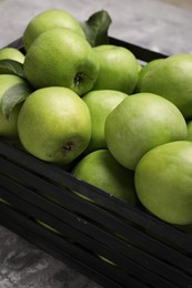 Photo of Fresh green apples in black crate on grey textured table, closeup