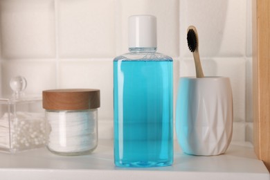 Photo of Bottle of mouthwash, toothbrush, cotton buds and pads on white shelf in bathroom