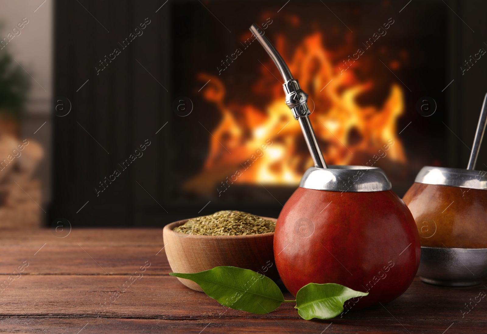 Image of Calabash with mate tea and bombilla on wooden table near fireplace. Space for text