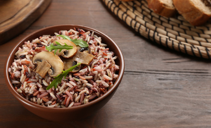 Photo of Delicious brown rice in bowl on wooden table