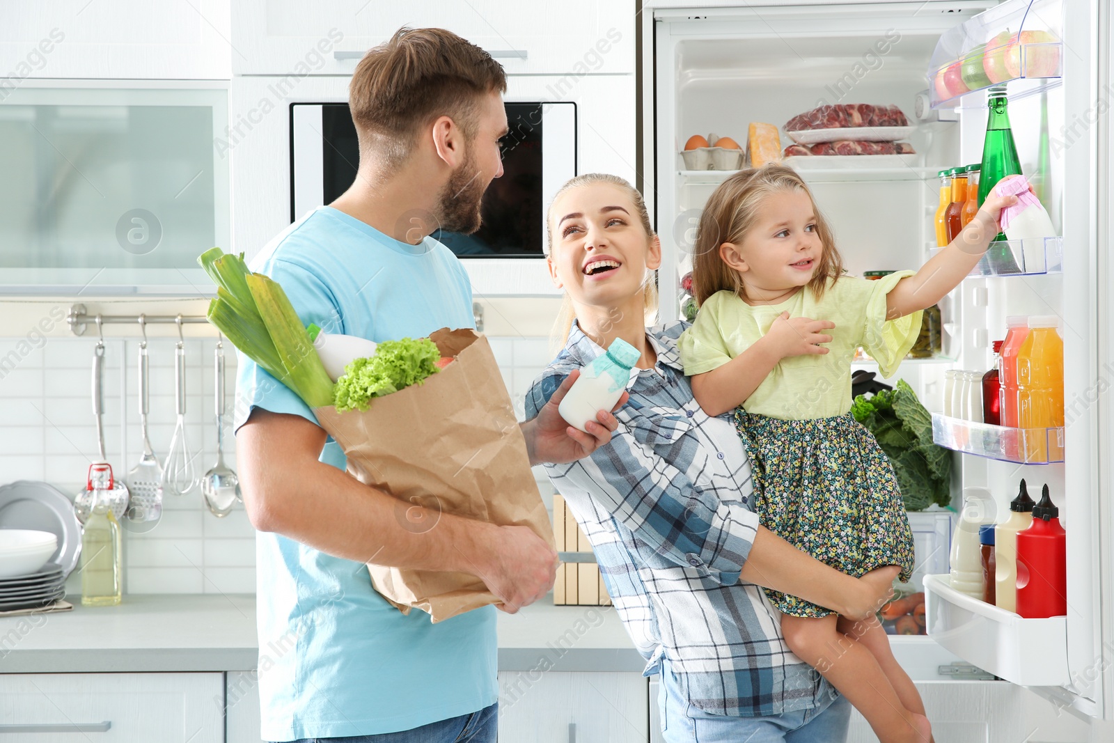 Photo of Happy family putting products into refrigerator in kitchen